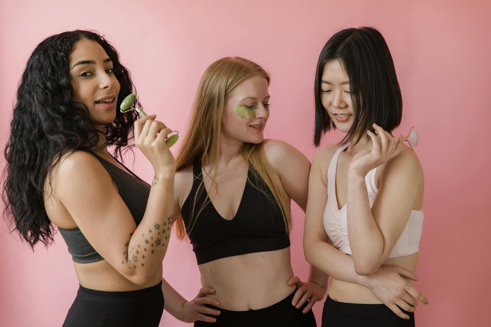 Three diverse women enjoying skincare routine with jade rollers in a studio.